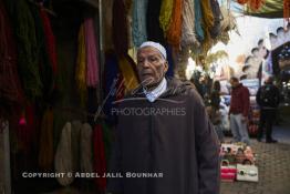 Image du Maroc Professionnelle de  Mohammed Ennaji âgé de soixante-dix ans, pose devant son atelier à Marrakech, il a commencé à pratiquer ce métier de teinturier à l’âge de dix ans, cela lui fait soixante ans de métier un des plus ancien voir le vétéran des teinturiers, son atelier est situé au centre du Souk des Teinturiers, appelé souk Sebbaghine, l'un des plus pittoresque de Marrakech situé dans la Médina, non loin de la source Mouassine, où quelques petits ateliers pratiquent encore de nos jours la teinture traditionnelle. Ce lieu très prisé des touristes et amateurs photos qui désire ardemment des images extrêmement colorées. Avec le temps il est devenu presque une des attractions touristique qui vaut le détour. Derrière Si Mohammed Ennaji des écheveaux de laines sèchent au soleil suspendu en l’air ou le long des murs, le 8 Décembre 2018. (Photo / Abdeljalil Bounhar) 